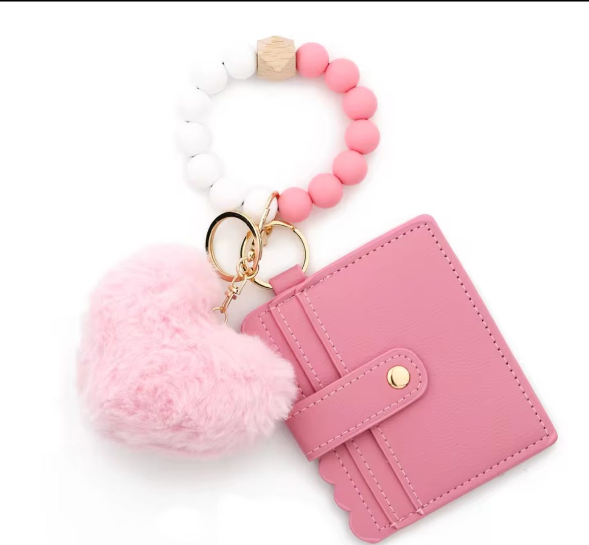 Pink keychain silicone wristlet with heart-shaped pom-pom and cardholder on a black background