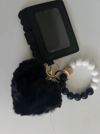Black wallet with white and black silicone beaded wristlet keychain featuring heart shaped pom-pom on a white background