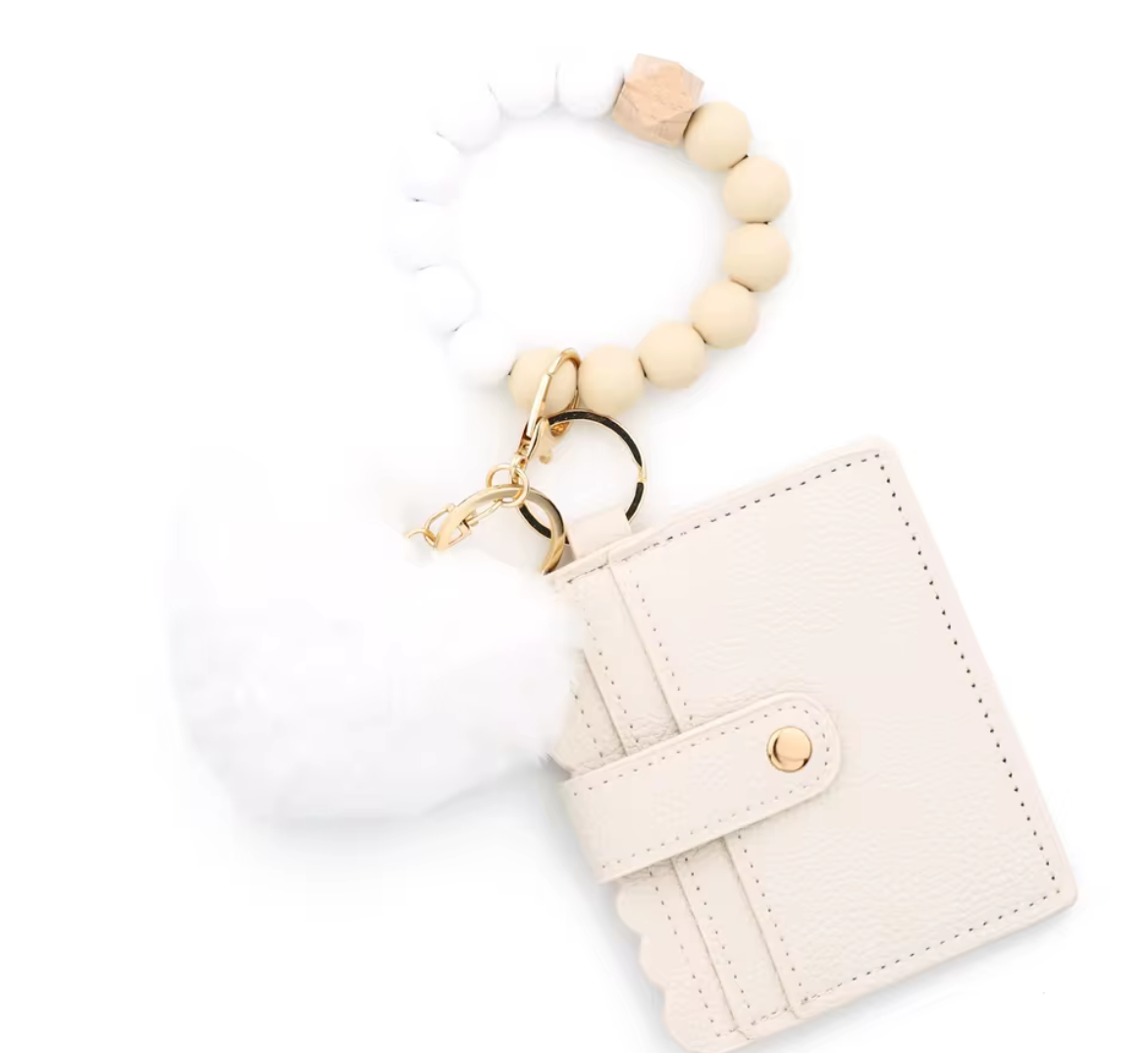 White and tan keychain 3 piece silicone wristlet with heart-shaped pom-pom and cardholder on a black background